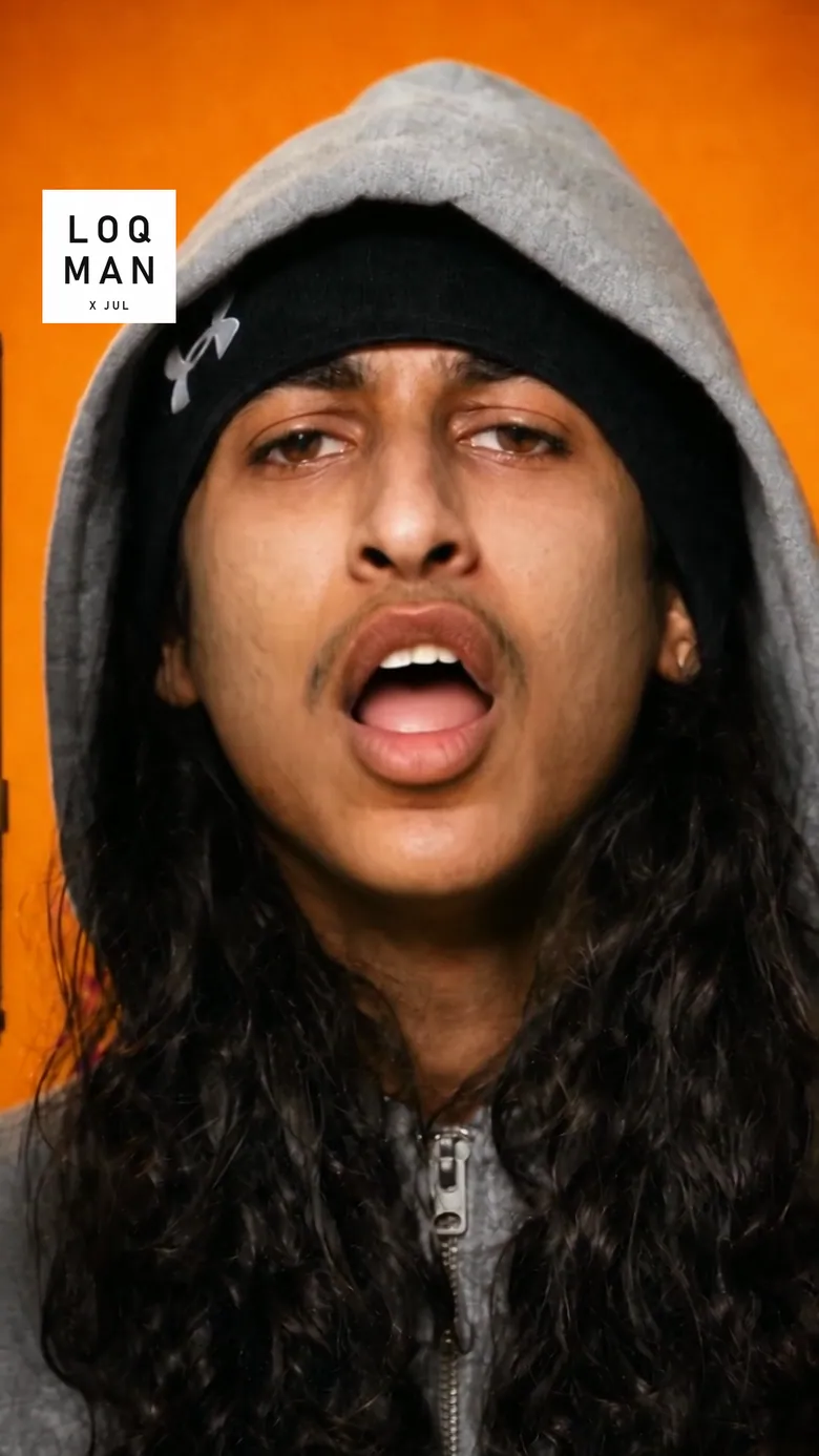 Image du montage à 54,4 secondes : gros plan de Loqman, capuche grise, regard caméra, bouche ouverte sur une syllabe.